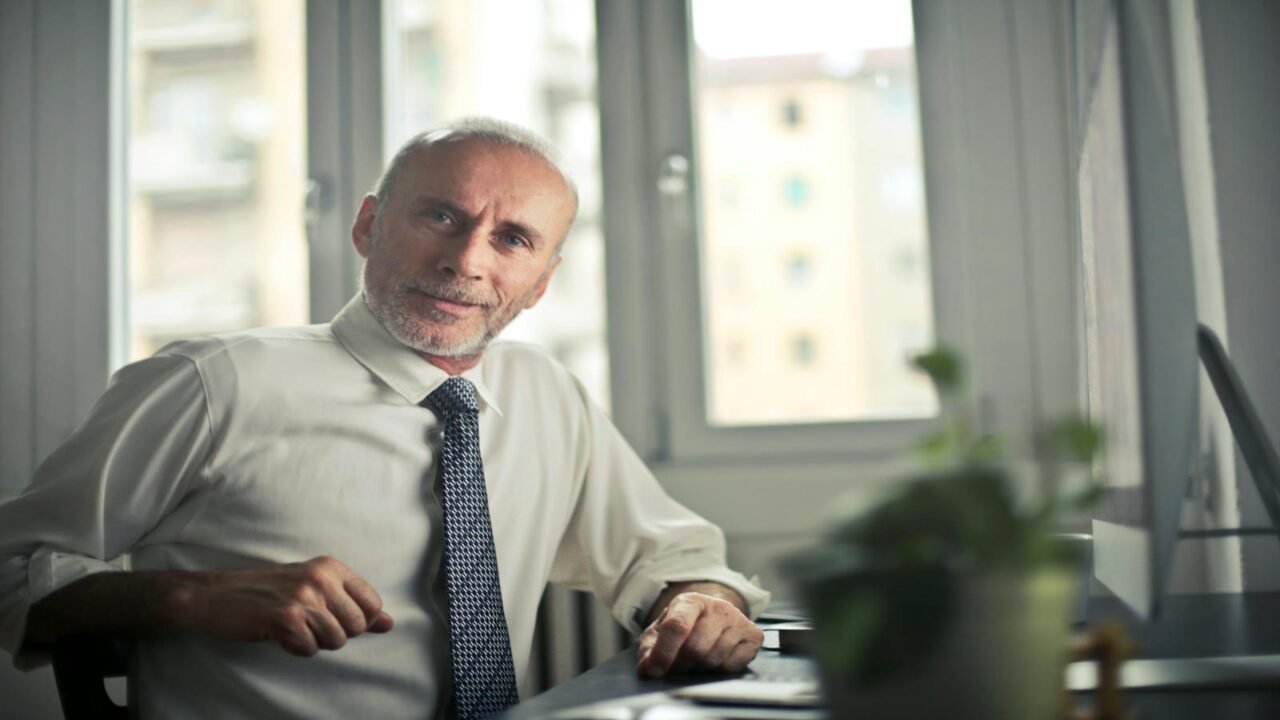 transformación organizacional, A mature man in professional attire smiling in an office setting.