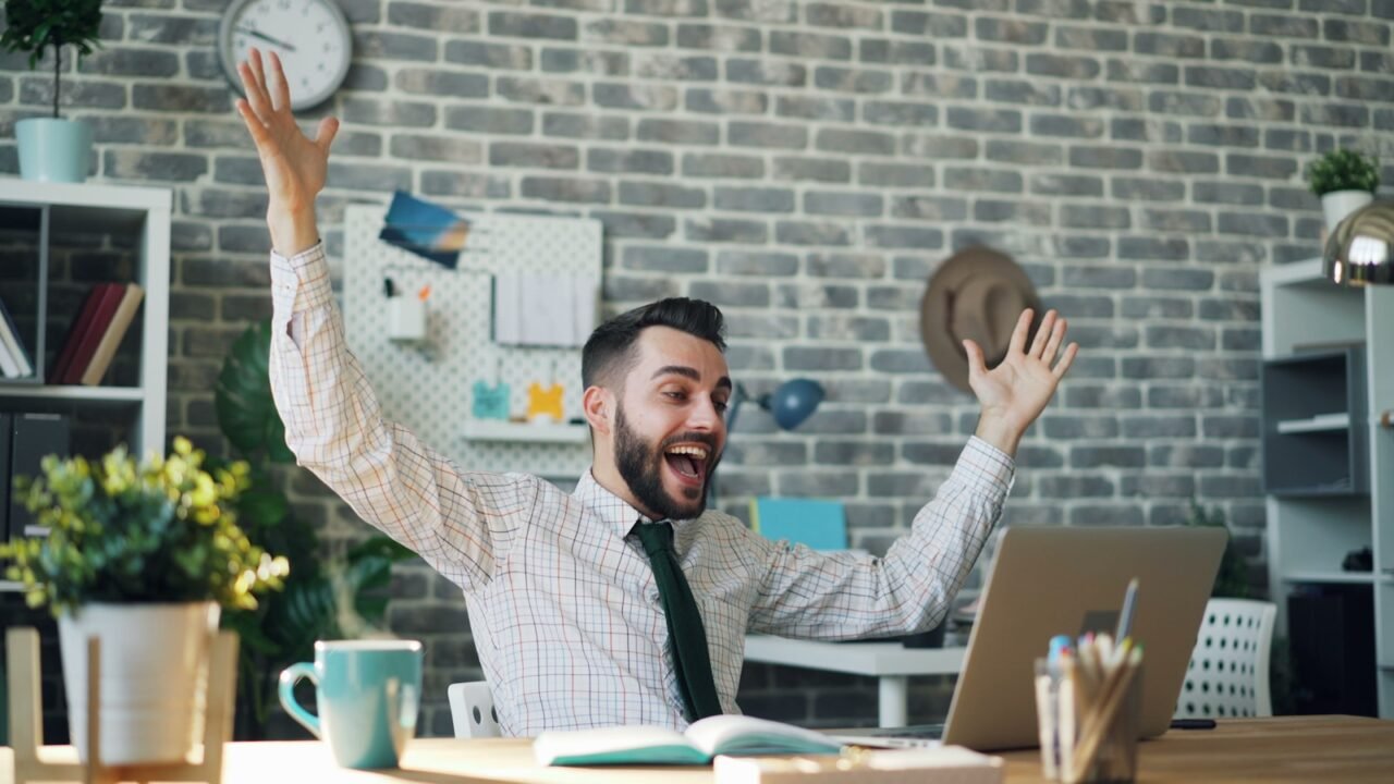 desarrollar habilidades blandas en tu empresa, a man sitting at a desk with his arms in the air