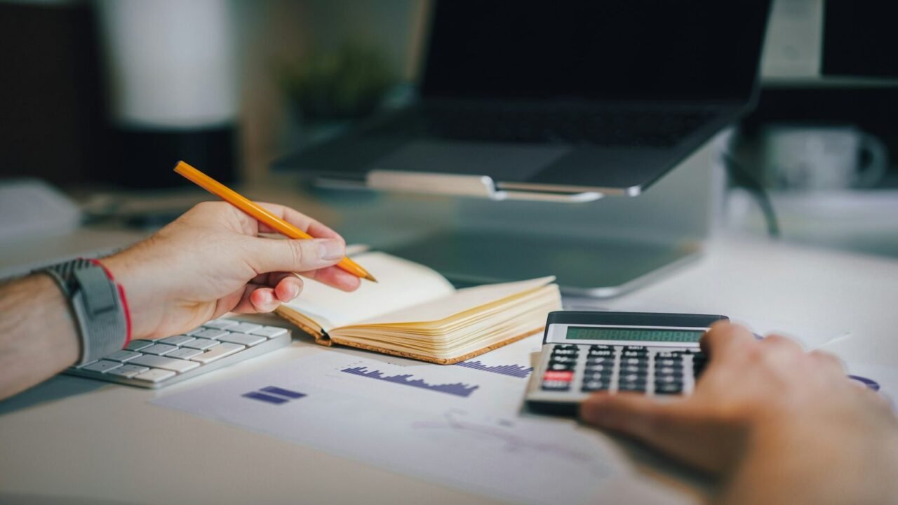 40% en costos operativos de TI, a person sitting at a desk with a calculator and a notebook