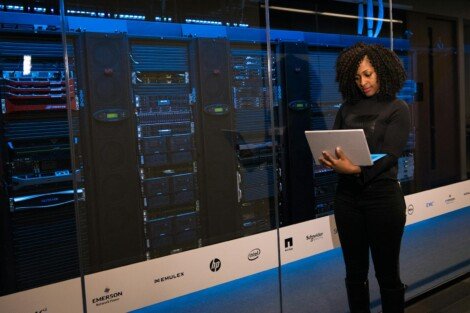 infraestructura tecnológica, A female engineer using a laptop while monitoring data servers in a modern server room.