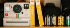 reinventarse para sobrevivir, A classic Polaroid OneStep Plus camera with film rolls on a wooden shelf, showcasing retro photography equipment.