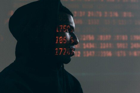 cuánto cuesta un ataque cibernético, Side profile of a man in a hoodie, surrounded by red code, depicting cybersecurity theme.