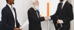 escucha activa en negociaciones comerciales, Three businessmen in suits having a meeting, shaking hands in front of a presentation chart.