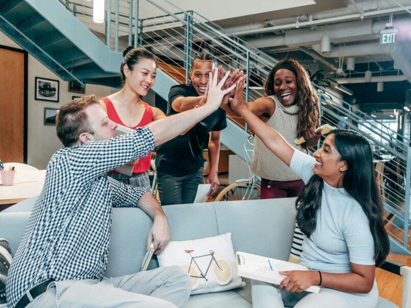 Team Building empresarial, A multicultural office team high-fiving and celebrating a successful collaboration.
