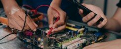 Tercerizar o contratar internamente los Servicios, Close-up of hands working on a motherboard using electrical tools and tester.