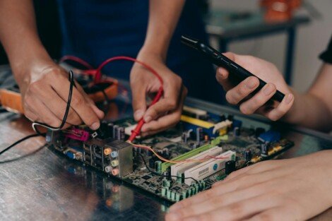 Tercerizar o contratar internamente los Servicios, Close-up of hands working on a motherboard using electrical tools and tester.